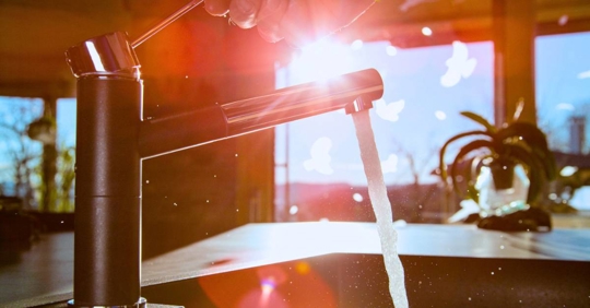modern kitchen faucet with water running against a sunny background